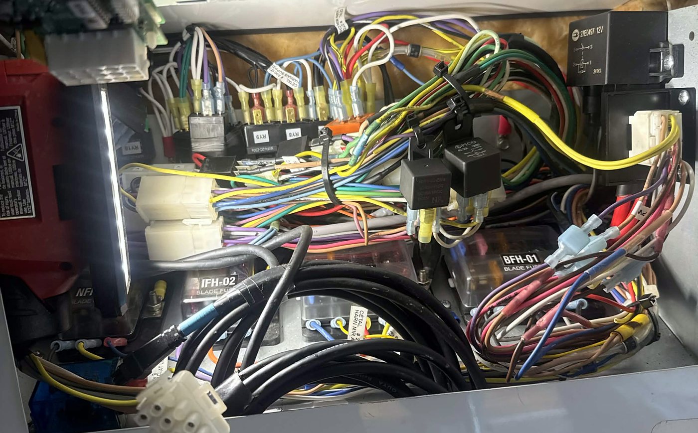Overhead electrical panel crammed with loose add-on relays, splices and coiled cable