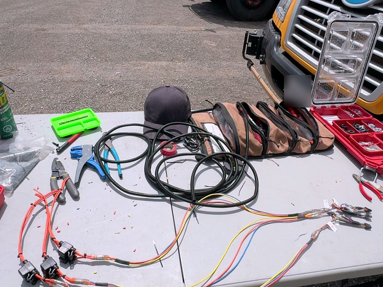 Fused harnesses built on a work table beside a row of school buses